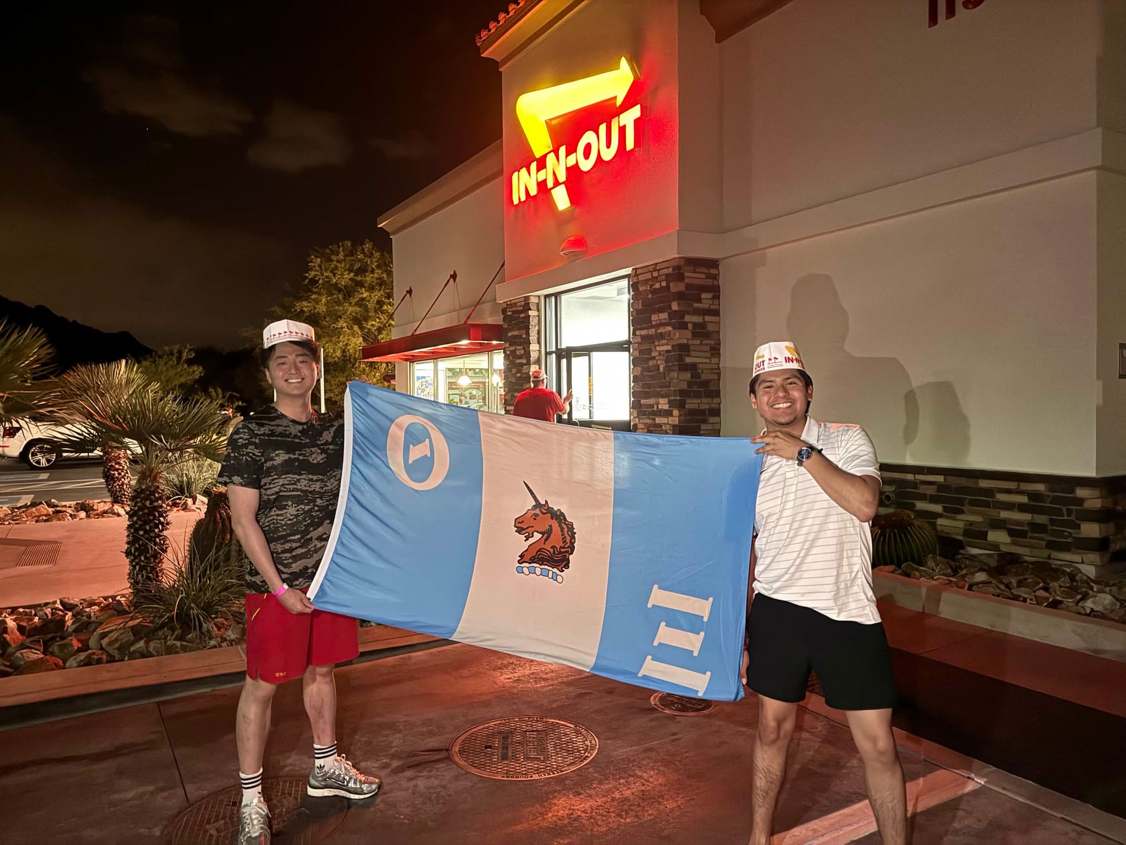 Two people holding a blue-and-white Theta Xi flag outside at night