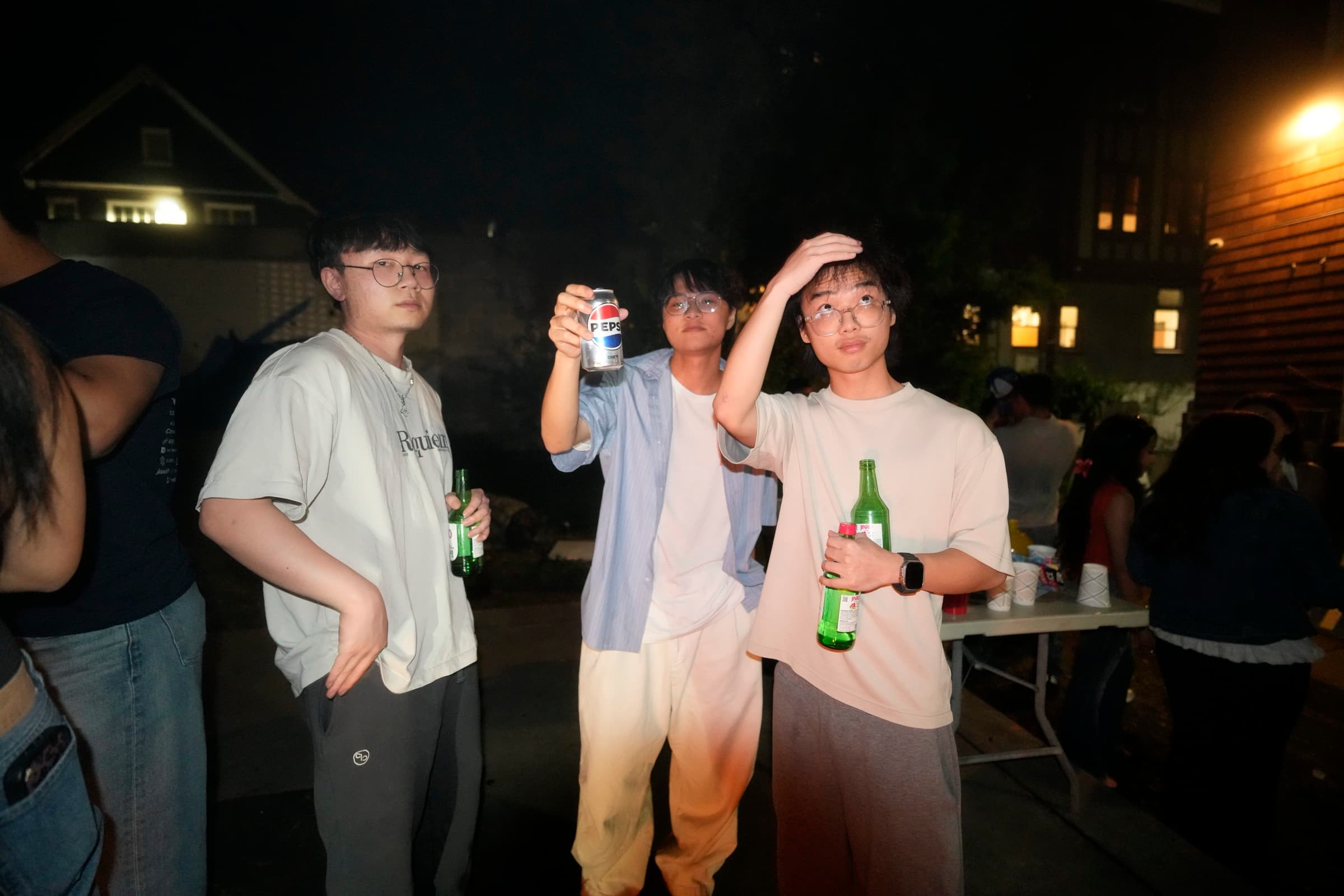 Three people holding drinks during an outdoor evening gathering